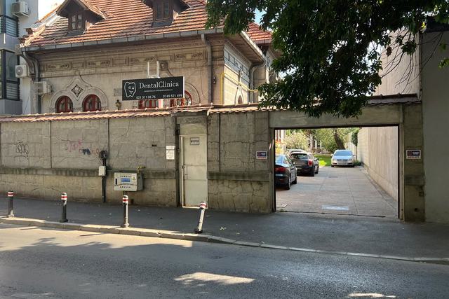 DentalClinica văzută din Strada Matei Voievod: casa cu acoperiș de țiglă, firma neagră DentalClinica și poarta de acces în curte